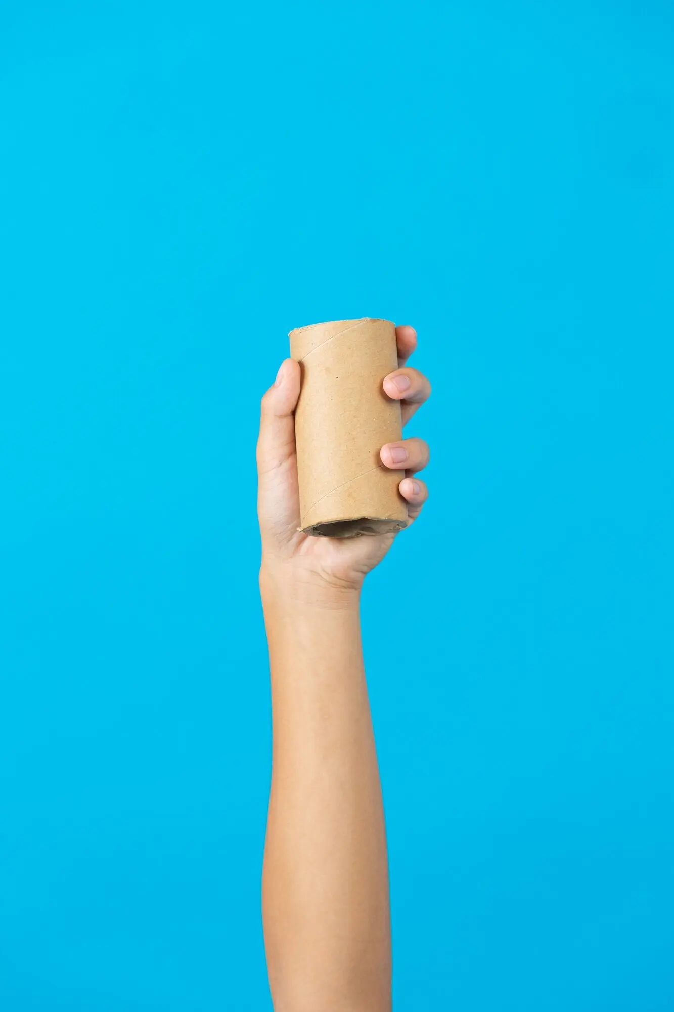 Una mano sostiene el núcleo usado de papel tisú sobre un fondo azul.